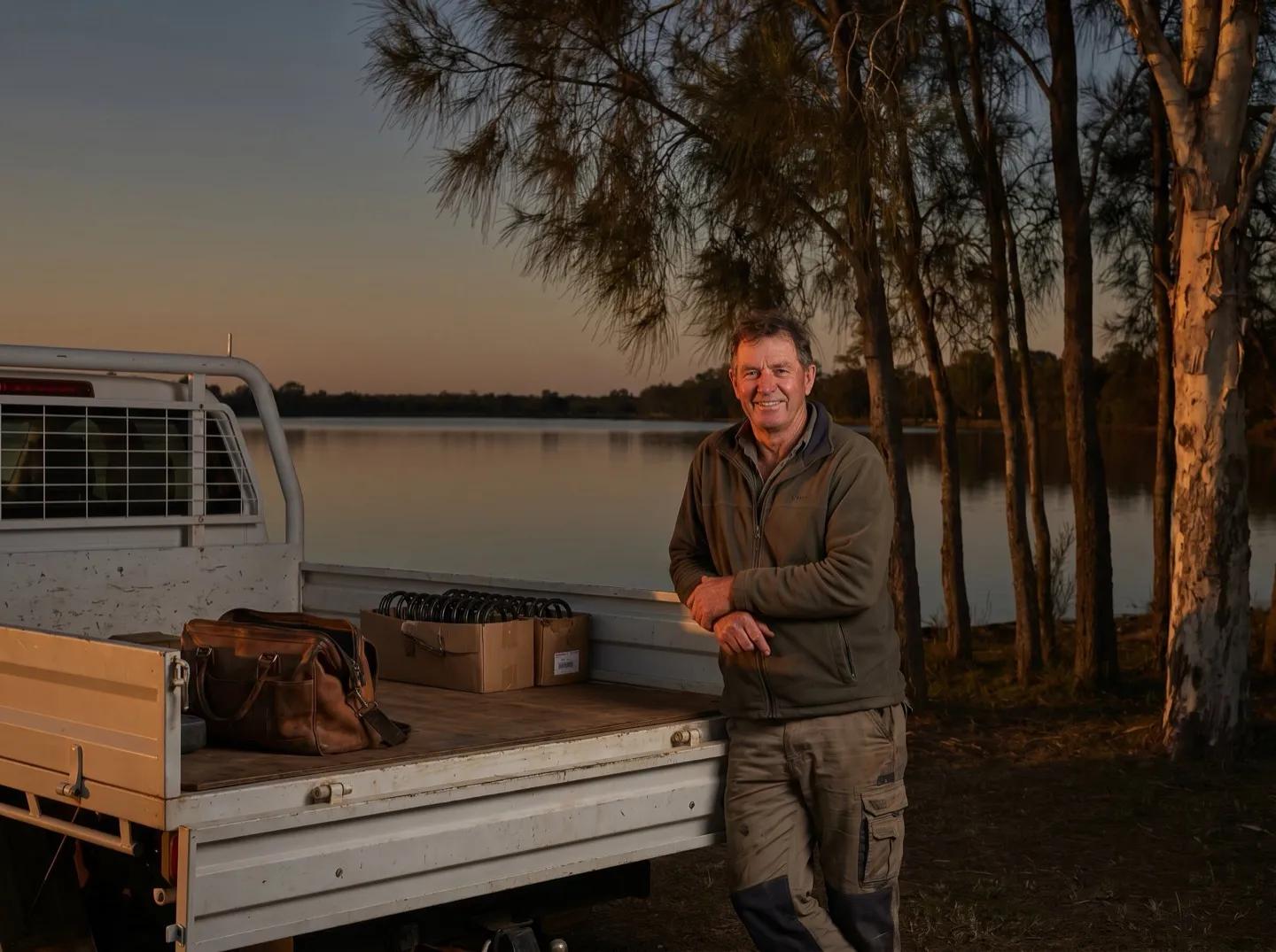 A garage door tradesman standing at the tailgate of his ute by the lake at dusk, springs boxed in the tray